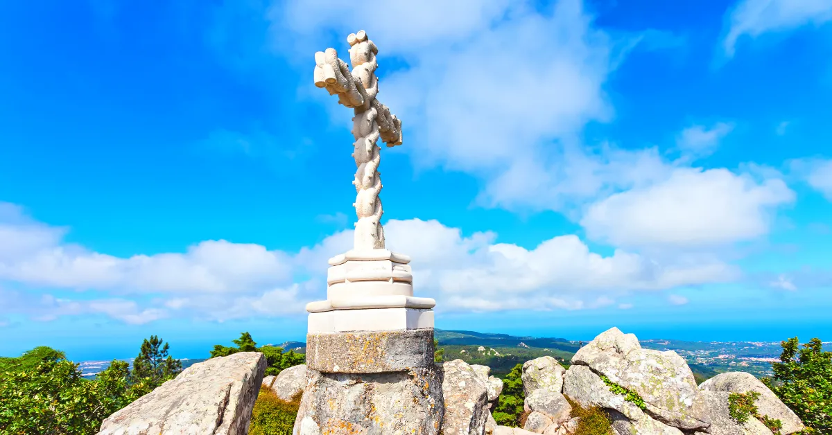 white ornate cross statue in front of view out from pena palace hiking near lisbon