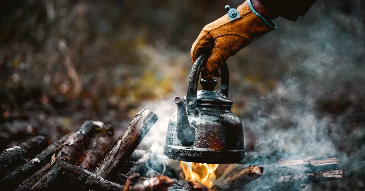 camp kettle held by glove over fire