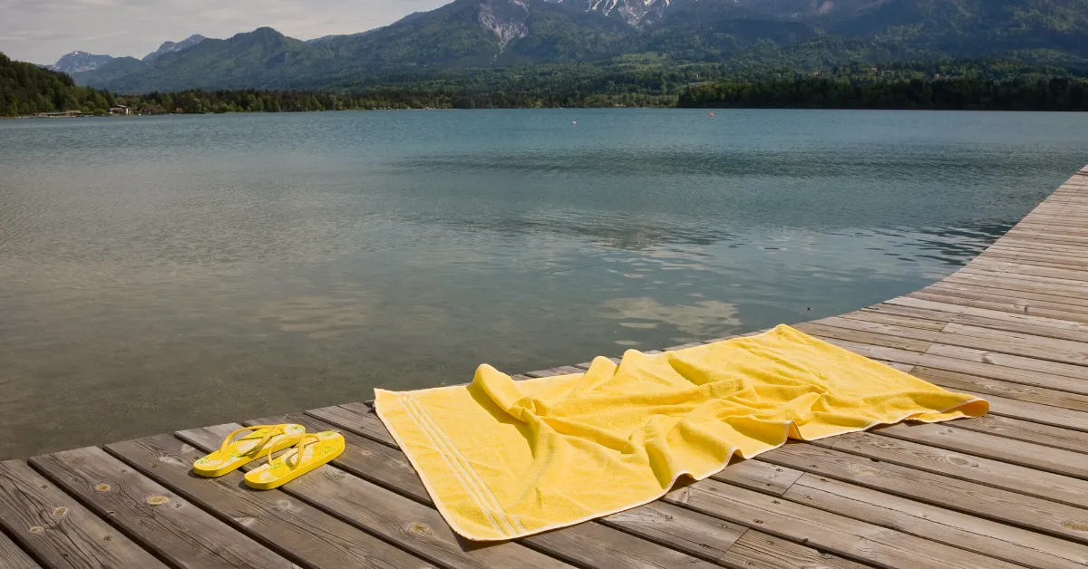 yellow camping towel with flip flops on dock in front of lake with mountain behind