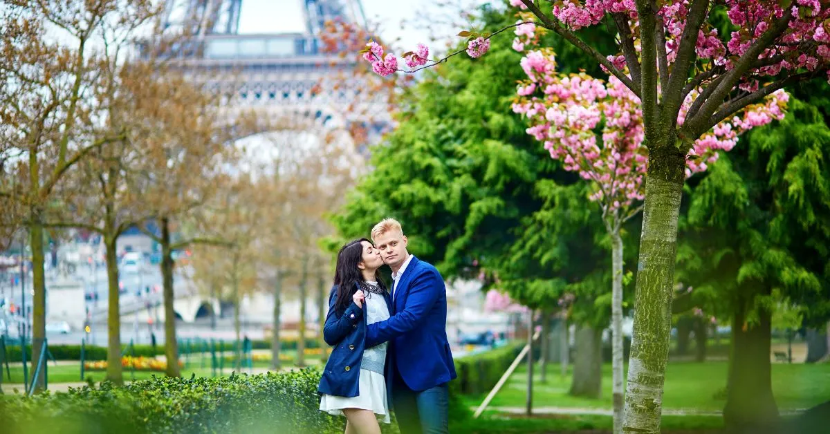 couple kissing in park in front of the eiffel tower